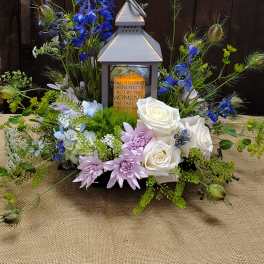 Lantern centerpiece surrounded by white roses, lavender blooms, and blue flowers