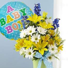 Yellow lilies and white daisies in a green pot with blue polka dot bow and baby boy balloon