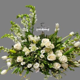 White floral arrangement with roses, lilies, and a clear cross centerpiece