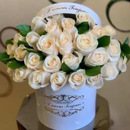 White roses arranged in a round white hatbox with green leaves