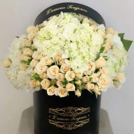 Cream roses and white hydrangeas arranged in a black hatbox