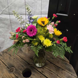 Mixed bouquet in a clear glass vase with bright pink, yellow, and lavender flowers