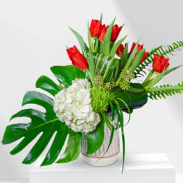 Red tulips and white hydrangea in a ceramic vase with large tropical leaves