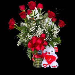 Red roses in a glass vase with a teddy bear holding a heart