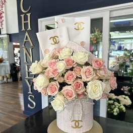 Pink and white roses arranged in a decorated hatbox with pearl accents