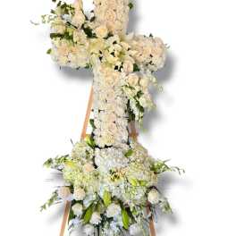 White floral cross on a wooden easel with roses and lilies