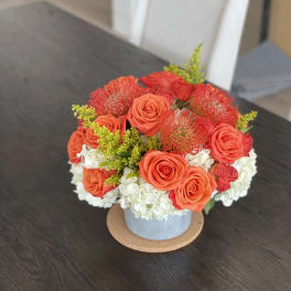 Orange roses and red pincushion blooms in a blue vase