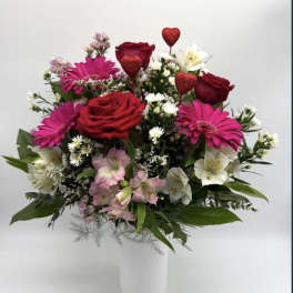 Mixed bouquet of red roses, pink daisies, and white lilies in a white vase