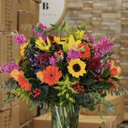 Colorful mixed bouquet in a clear glass vase with lilies and sunflowers