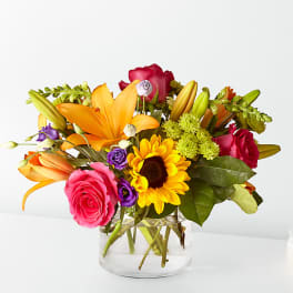Mixed bouquet of roses, lilies, and a sunflower in a clear glass vase