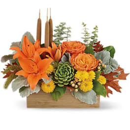 Orange lilies and yellow blooms in a wooden box with candles