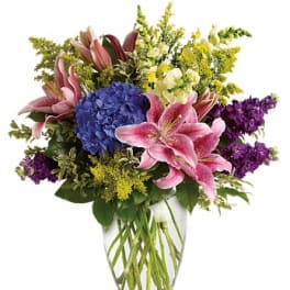 Bouquet of pink lilies, blue hydrangea, and purple flowers in a clear glass vase