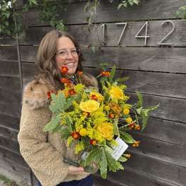 Woman holding a yellow and orange bouquet in a glass vase
