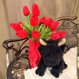 Red tulips in a glossy red vase beside a black plush bull