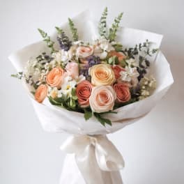 Bouquet of peach and blush roses with white flowers wrapped in white paper