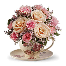 Pink and cream roses arranged in a floral teacup with saucer