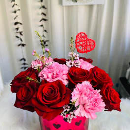Red roses and pink carnations in a heart-decorated vase with a red heart pick