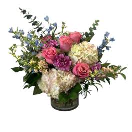 Pink roses and hydrangeas in a glass vase with blue accent flowers