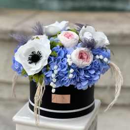 Blue hydrangeas with white and pink flowers in a black hatbox