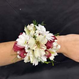 White floral wrist corsage with burgundy ribbon on a person’s wrist