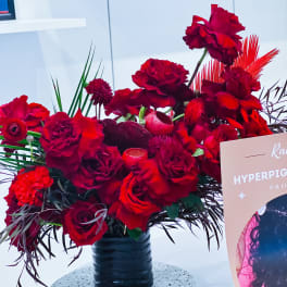 Red rose arrangement in a black vase with tropical foliage accents