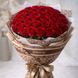 Large bouquet of red roses wrapped in patterned paper with a gold ribbon