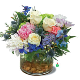 Low glass vase of cream roses, pink peony, white mum and blue flowers in a compact mixed bouquet