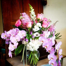 Pink and lavender orchids with roses in a glass vase