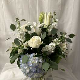 White lilies, roses, and blue hydrangea in a glass vase