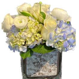 White roses and pale blue hydrangeas in a square glass vase