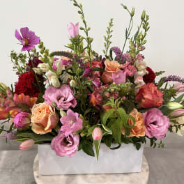 Large mixed bouquet in a white rectangular vase with pink, peach, and red blooms.