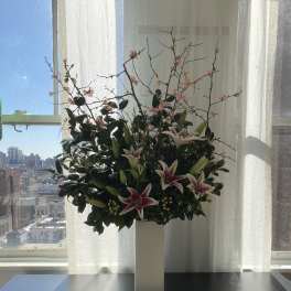 Tall floral arrangement with pink lilies and flowering branches in a white pedestal vase