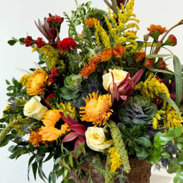 Mixed bouquet in a woven basket with yellow, orange, red, and cream flowers