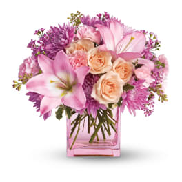 Pink lilies, peach roses, and lavender flowers arranged in a pink glass cube vase