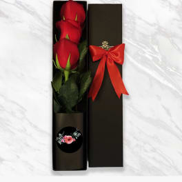 Three red roses in a black gift box with a red ribbon