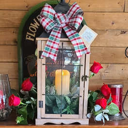 Lantern with candle, red roses, and plaid bow on a wooden shelf