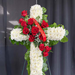 Tall white chrysanthemum cross with red roses and a red memorial ribbon on a metal easel.
