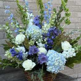 Basket arrangement of blue and white flowers with roses and hydrangeas