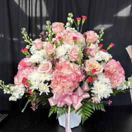 Pink roses and hydrangeas in a white vase with a pink ribbon