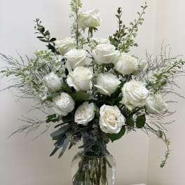 White roses arranged in a clear glass vase with airy greenery