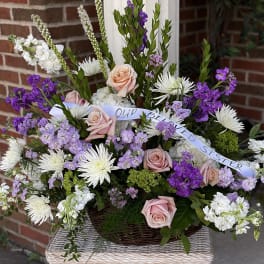 Basket arrangement of pink roses, white daisies, and purple flowers with a ribbon
