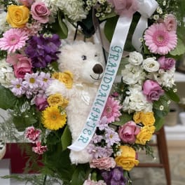 Heart-shaped floral wreath with a teddy bear and ribbon