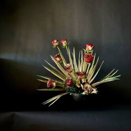 Red roses arranged with spiky dried foliage in a dark vase