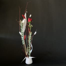 Tall red rose arrangement in a white vase with eucalyptus and white feathers