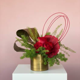 Red roses in a gold vase with green foliage and curved pink accents