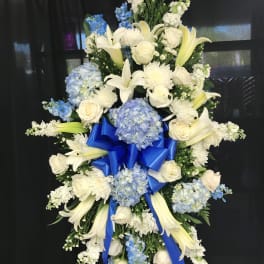 Standing floral spray with white lilies, roses, and blue hydrangeas on a black backdrop