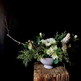 White chrysanthemum arrangement in a pale vase with greenery and branches