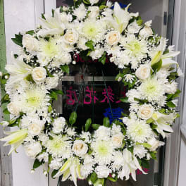 White floral wreath on a stand with roses, lilies, and chrysanthemums