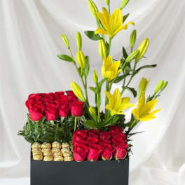 Red roses and yellow lilies arranged in a black box with chocolates