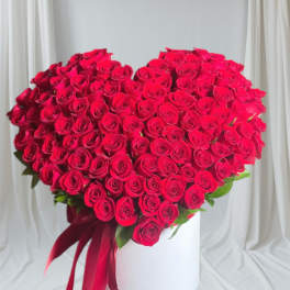 Heart-shaped bouquet of red roses with a red ribbon on a white pedestal